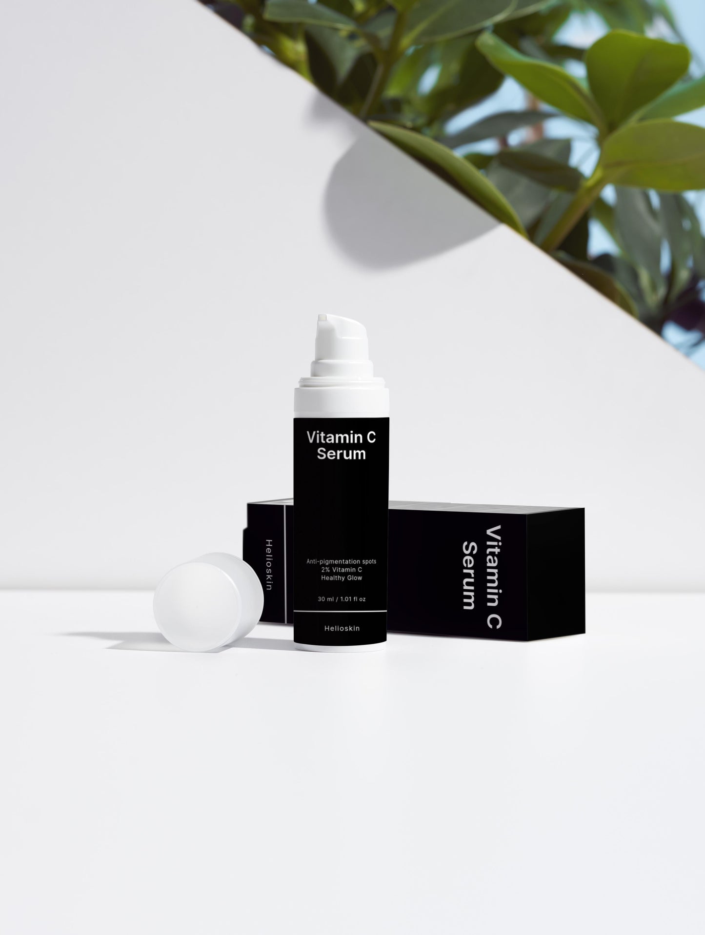 Vitamin C serum with packaging on a white surface with green leaves in the background