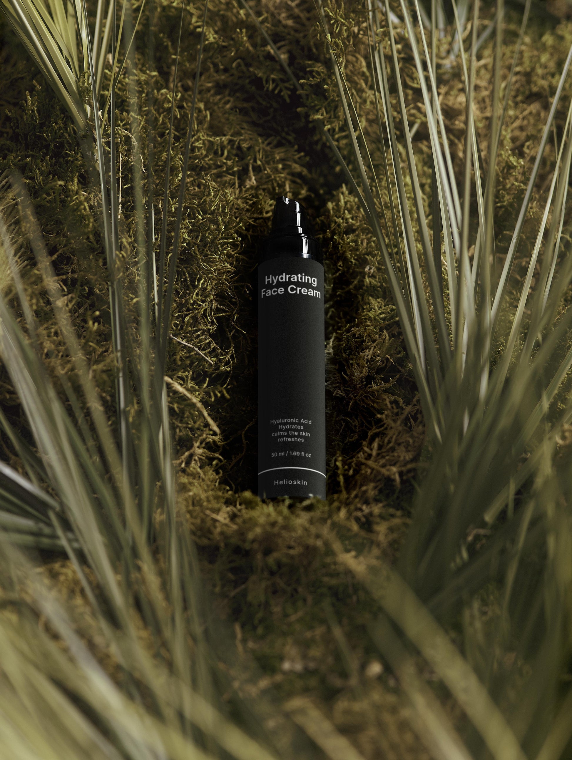 Black bottle of hydrating face cream surrounded by grass and moss