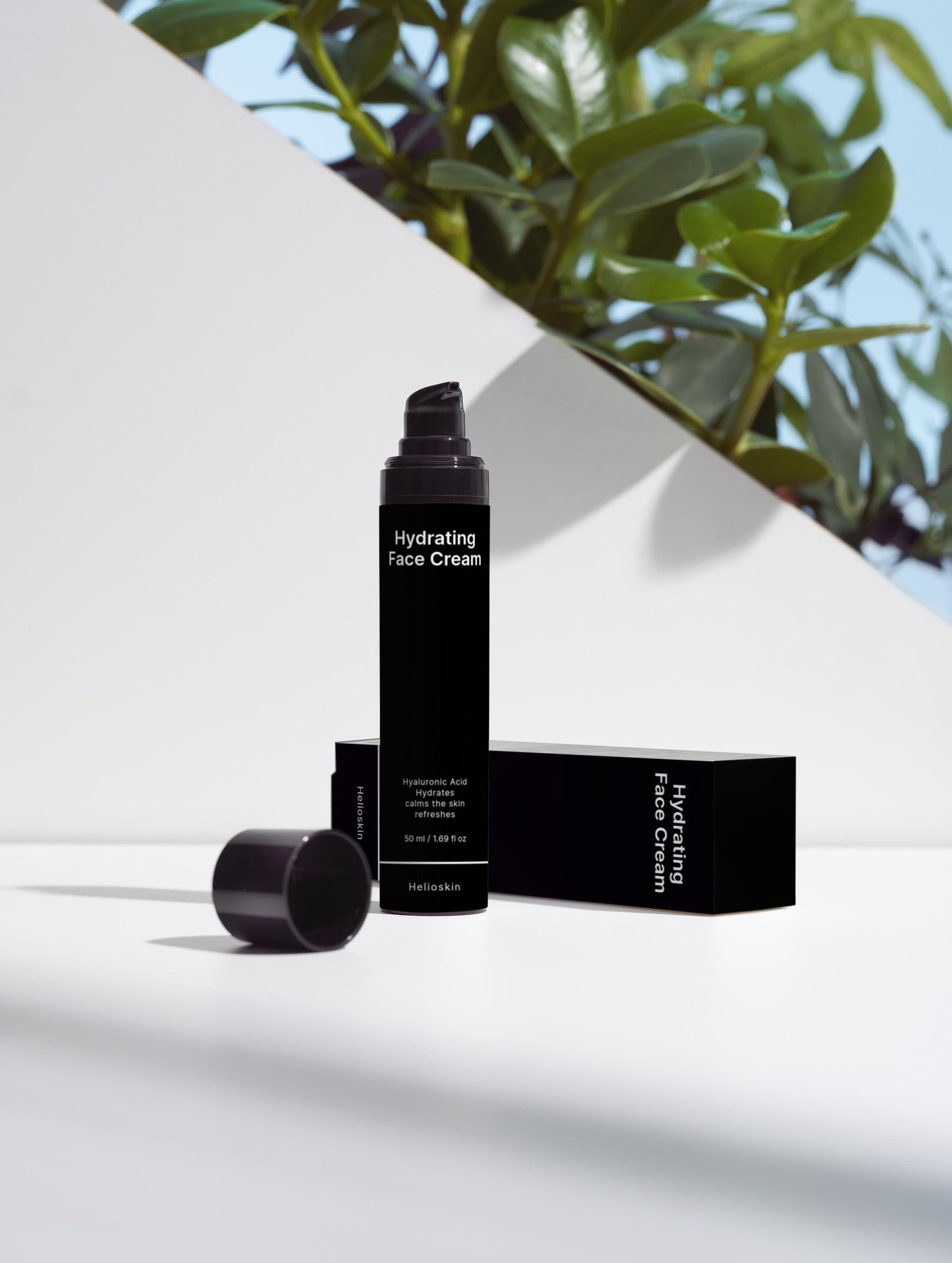 Black skincare product with packaging on a white surface with green leaves in the background