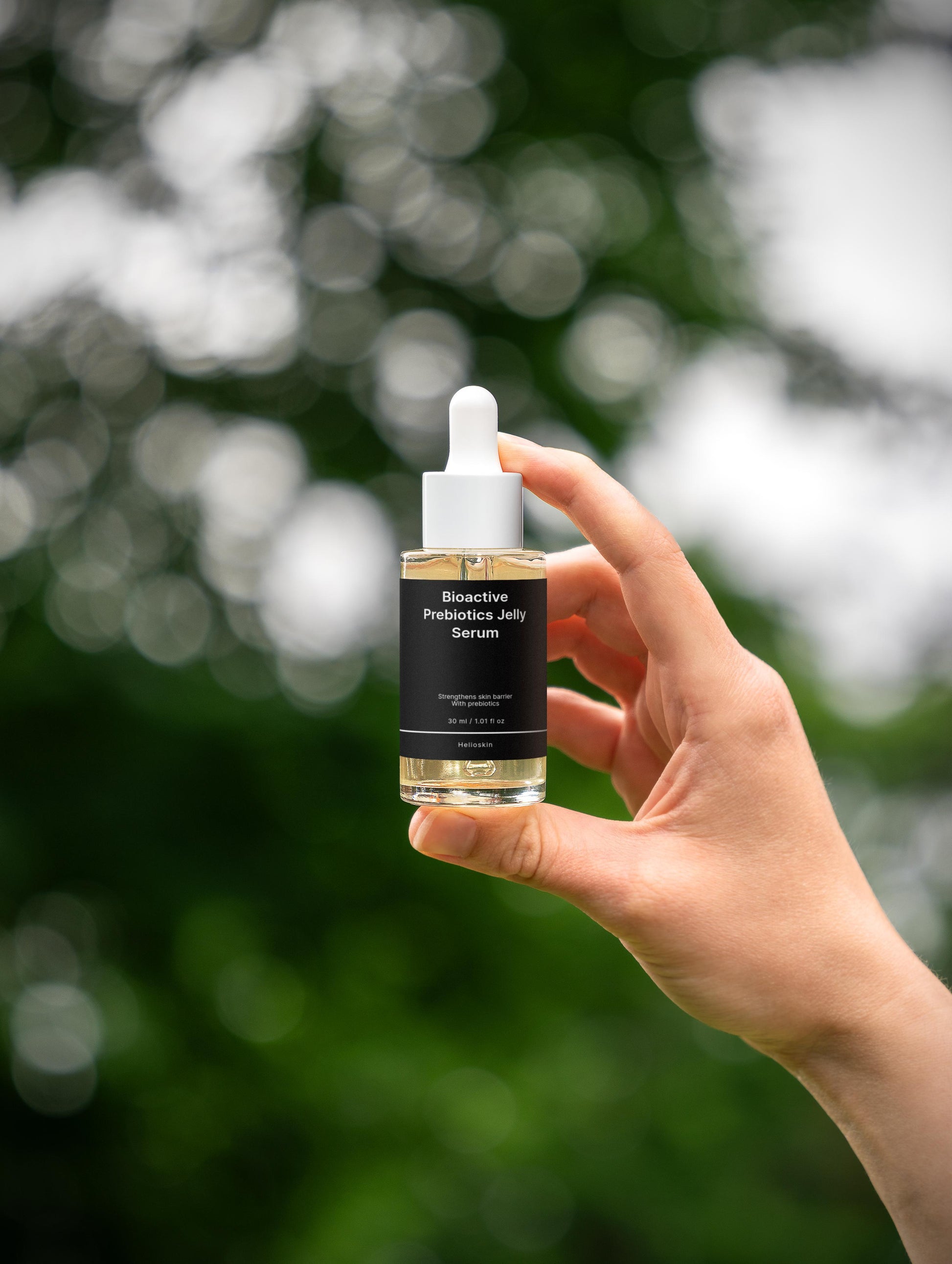 Hand holding a bottle of 'Bioactive Prebiotic Jelly Serum' against a blurred green background