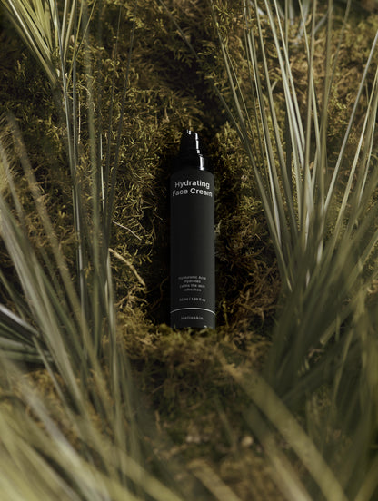 Black bottle of hydrating face cream surrounded by grass and moss