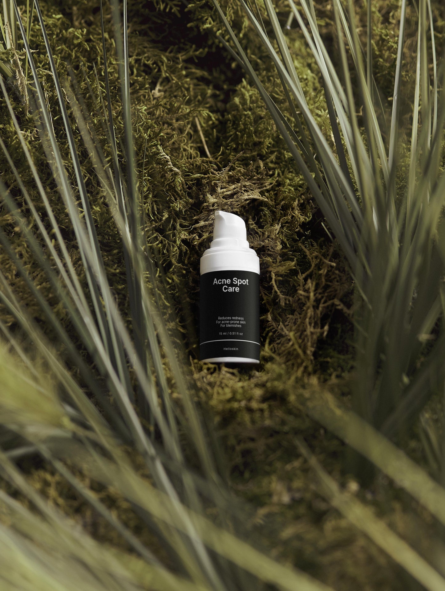 Skincare bottle labeled 'Acne Spot Care' on a natural background with grass and moss.